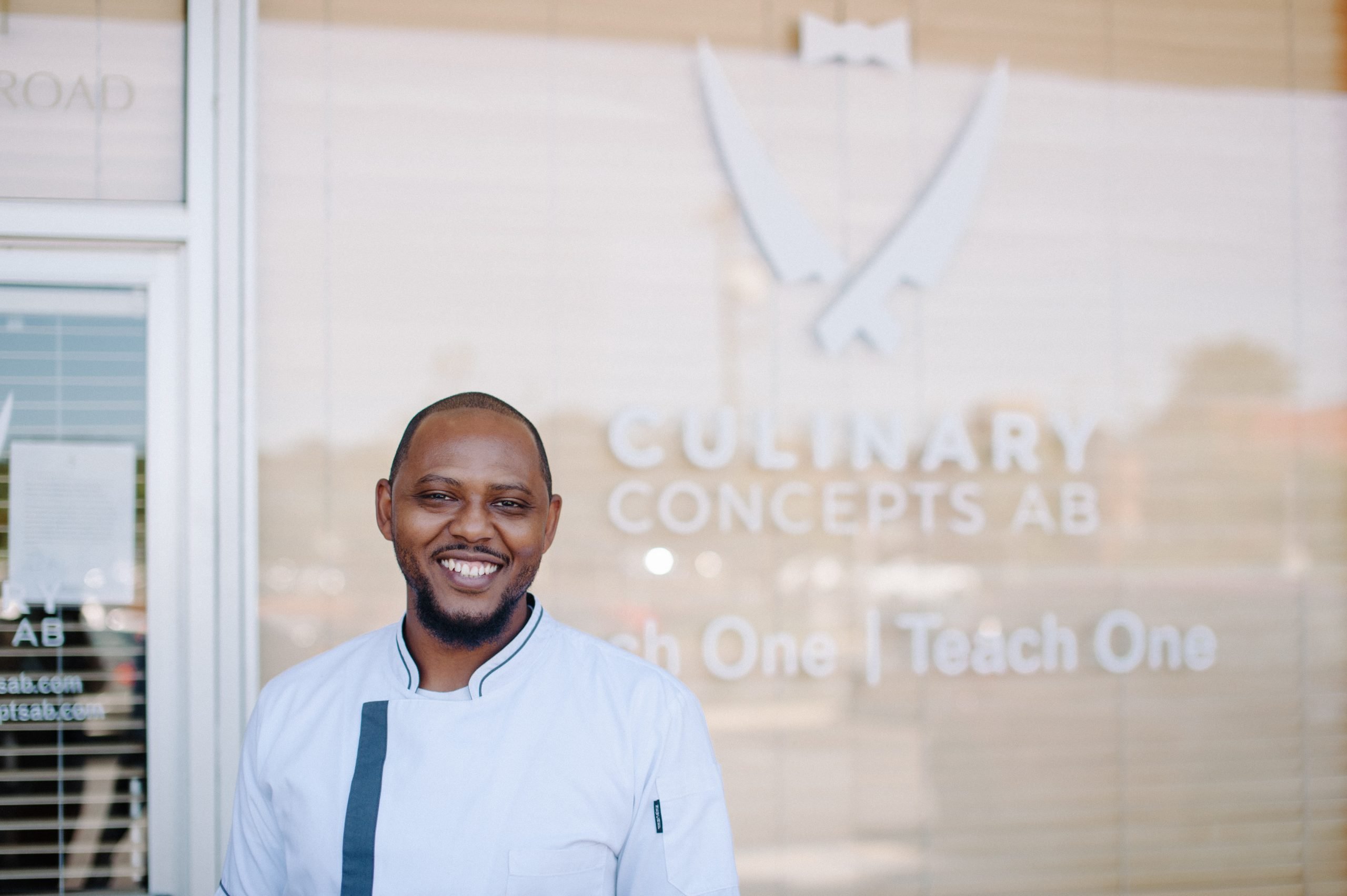 Man in chef coat in front of storefront window with sign "Culinary Concepts AB"