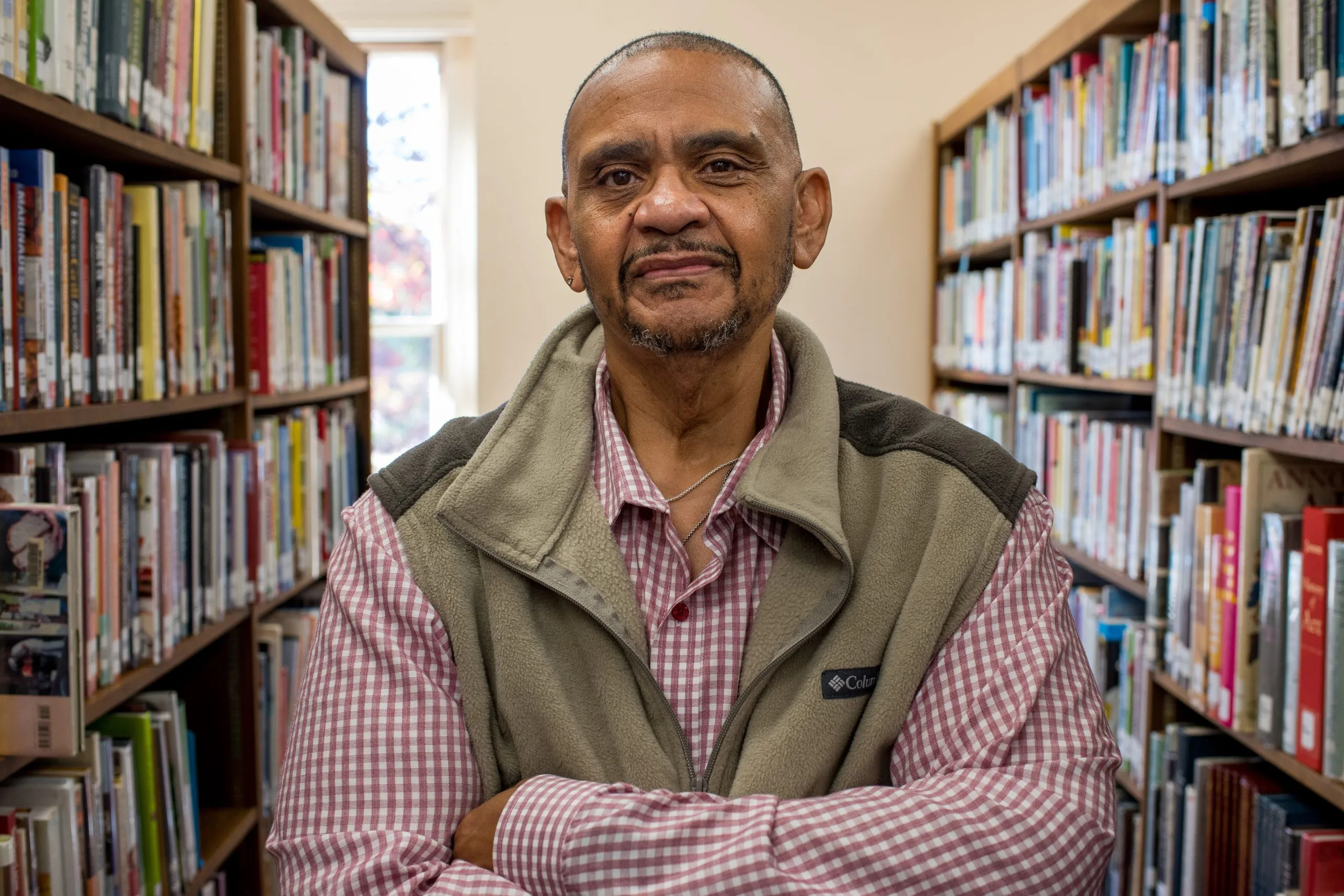 Man with arms folded poses between two stacks of books