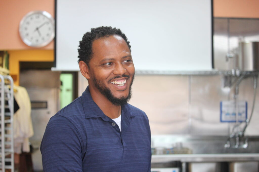 A man smiles with screen behind him.