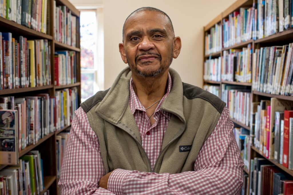 Man in vest stands between two shelves of books, looking at camera