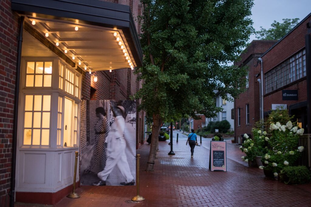 A brick lined street with a large format black and white photograph facing a lighted storefront.